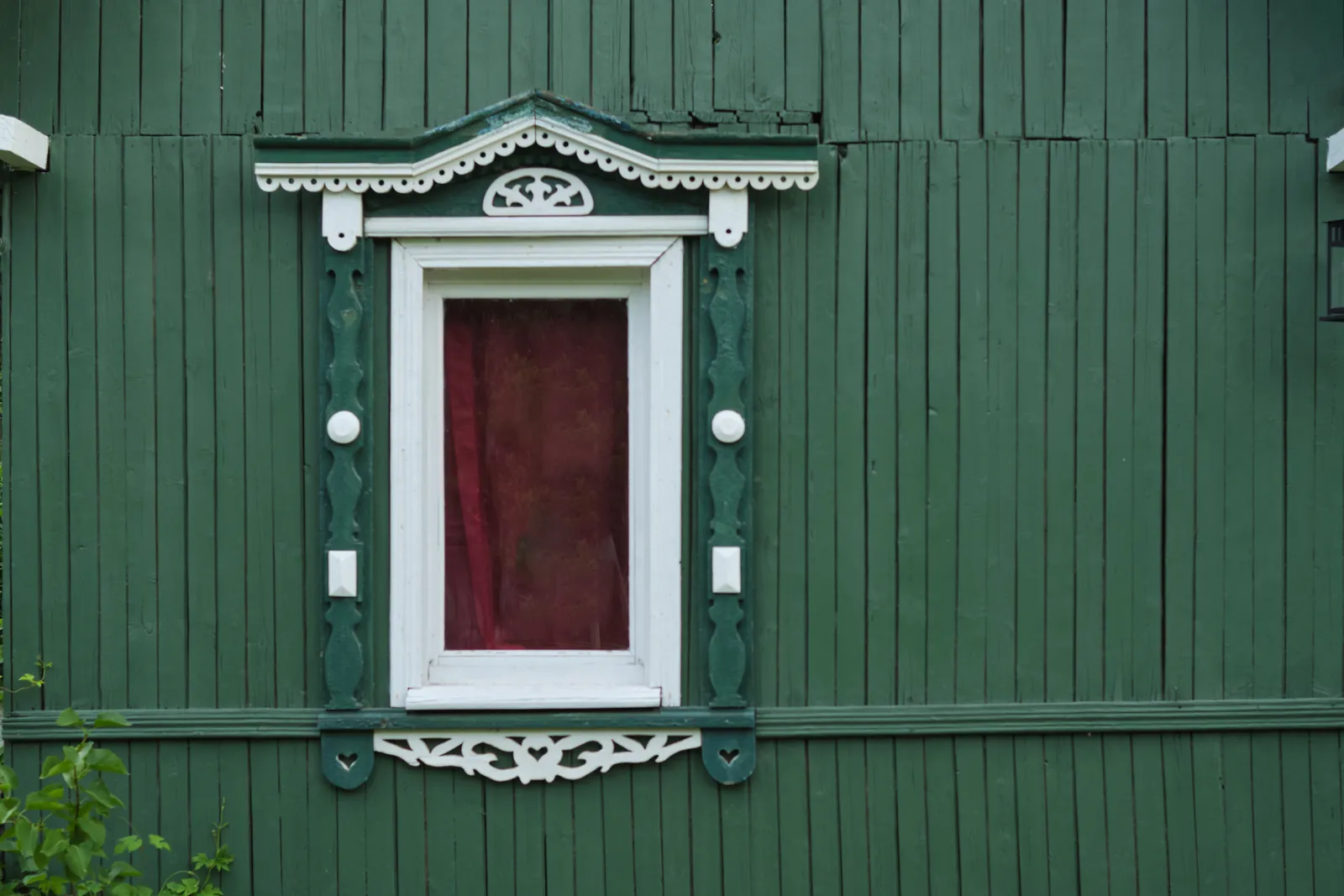 Green stained wooden wall with a red door and white trimmed window