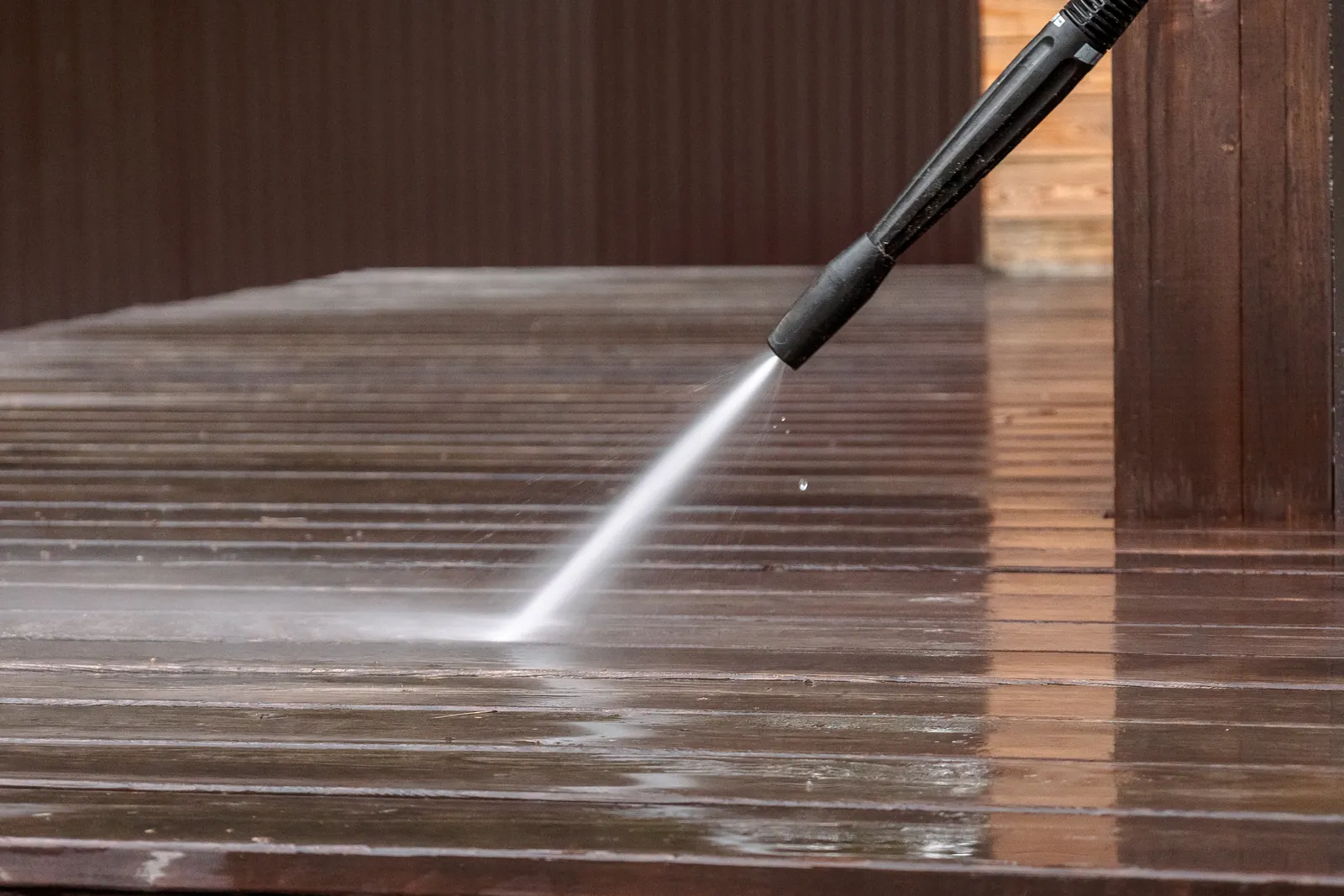 Pressure washer cleaning a wooden deck surface before staining