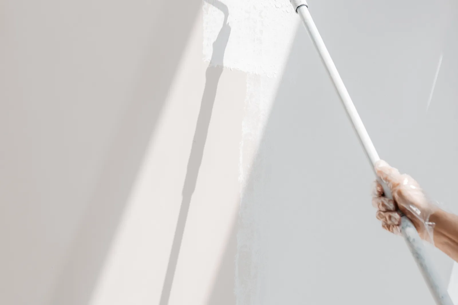Roller applying white paint to an interior wall