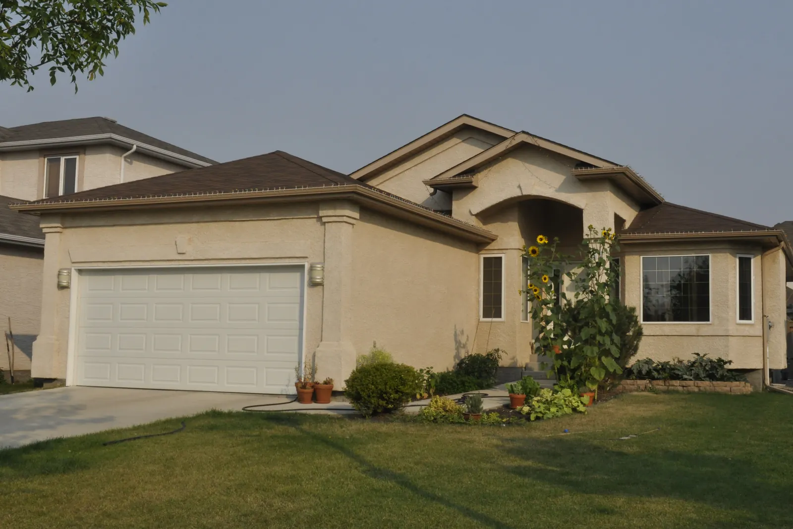 Tan single-storey house with a white garage door and green lawn