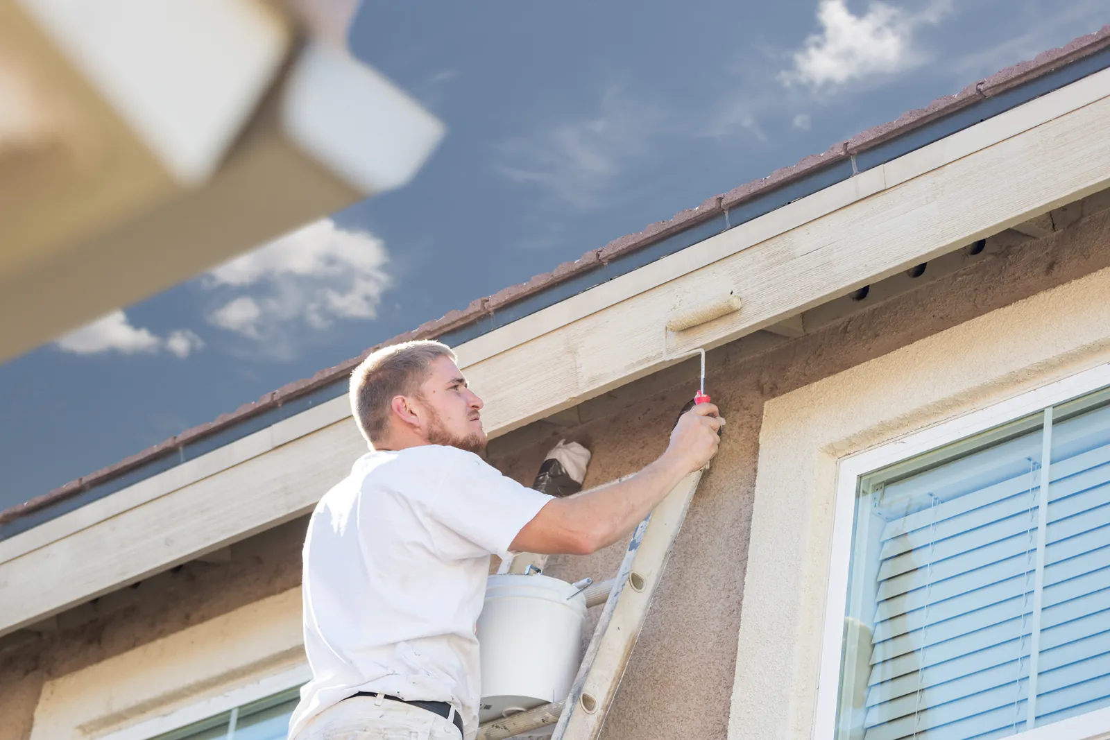 Painter on a ladder rolling paint onto house fascia