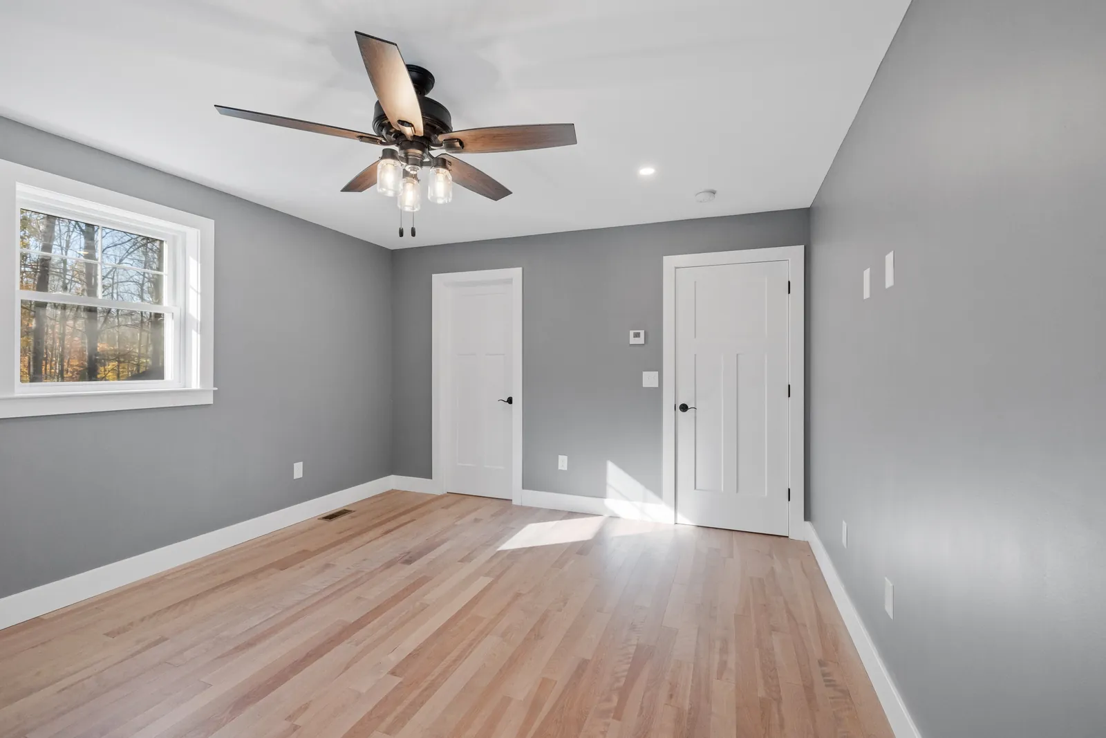 Bedroom with grey painted walls, hardwood floors and white doors